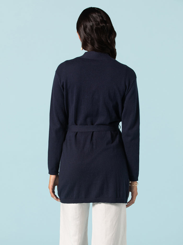 Navy long knit duster, back view, paired with white pants against a light blue background.