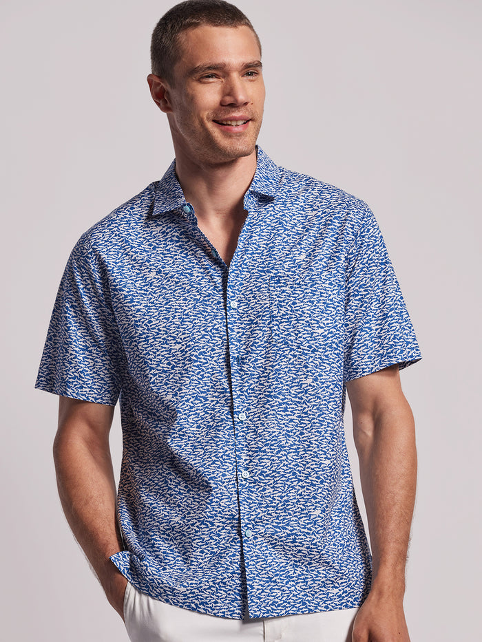 Blue shark-print cotton lawn button-up shirt, worn by man with one hand in pocket, front view.