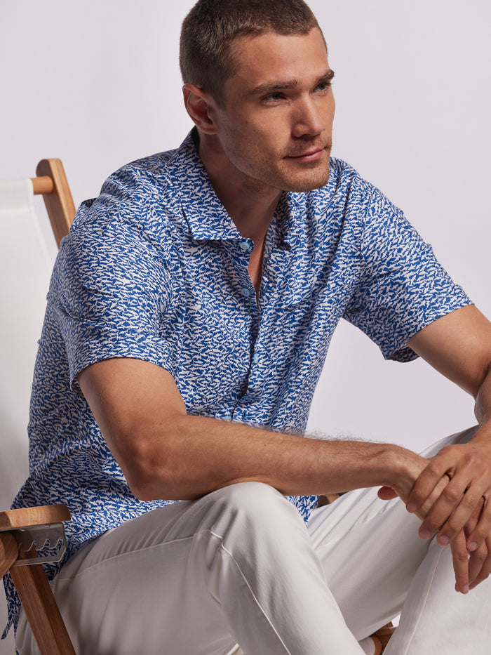 Blue shark-print cotton lawn shirt and white pants, seated side view.