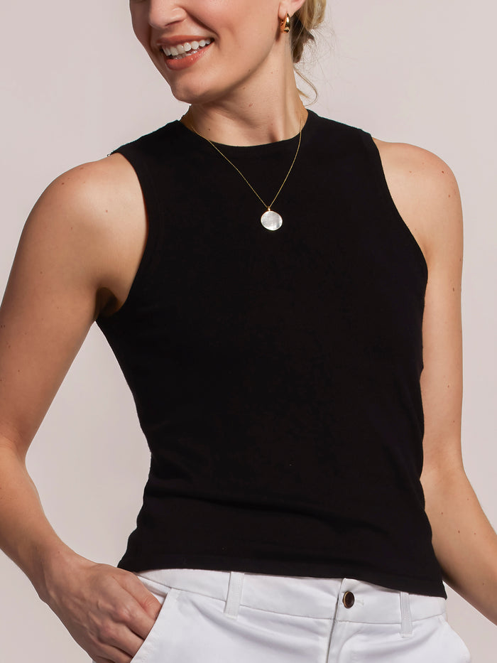 Black sleeveless knit tank top with white pants, front view, hand in pocket in both images.