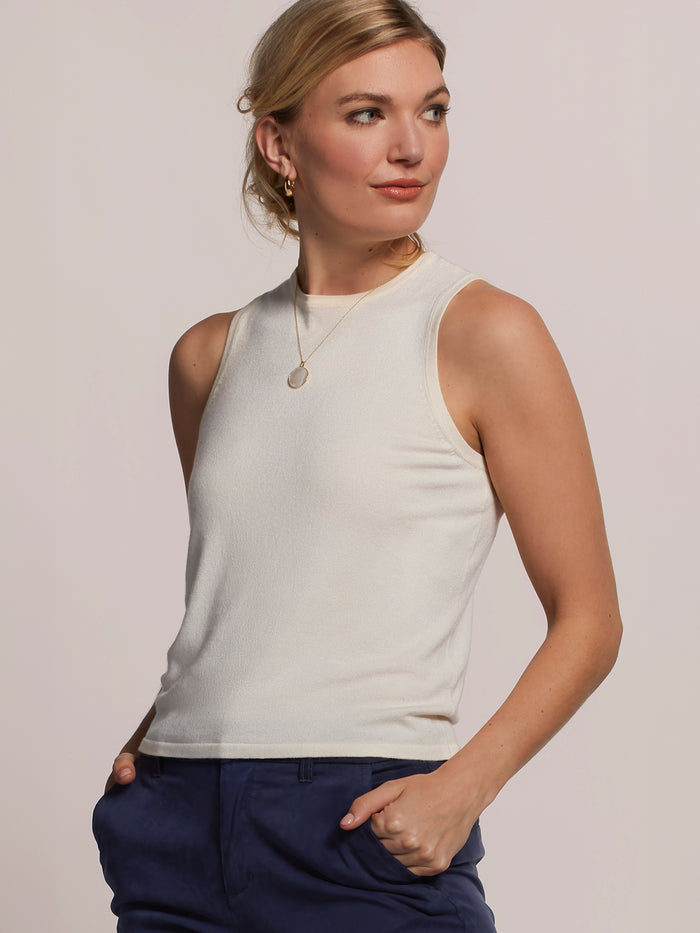 White sleeveless knit tank and solid blue pants, front view with modern styling detail.
