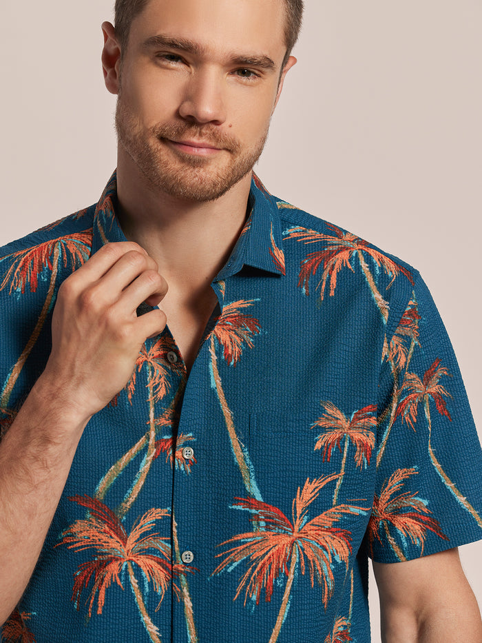 Blue Hawaiian shirt with red and orange palm tree print, front view.