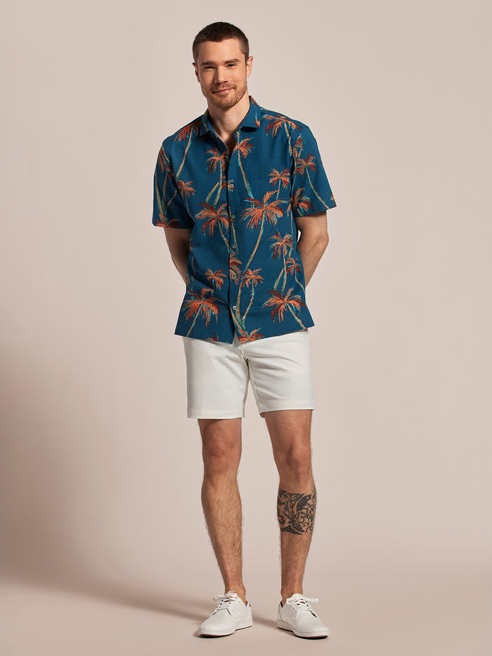 Blue palm-print short-sleeve shirt, white shorts, and shoes; hands behind the back.