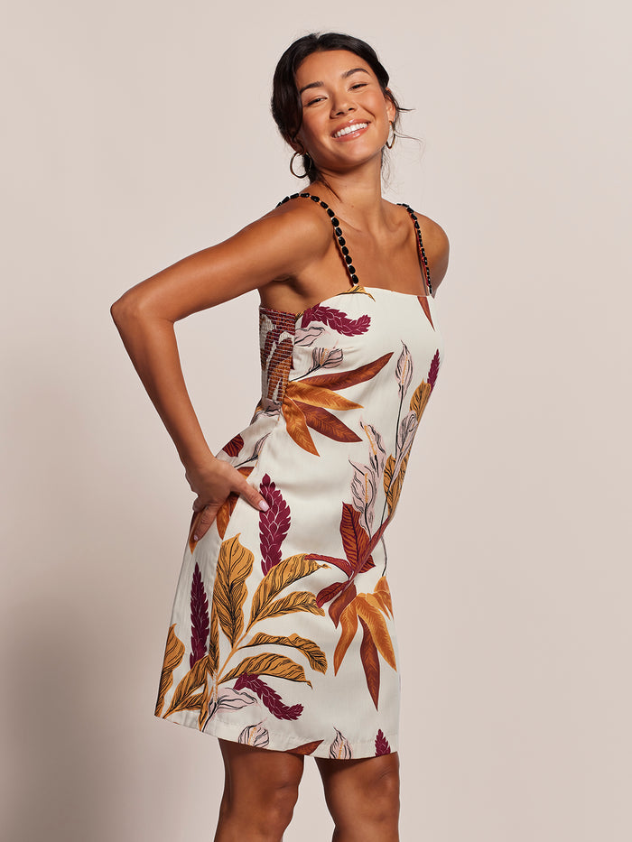 Light background, front view of woman smiling in colorful leaf-print midi dress.