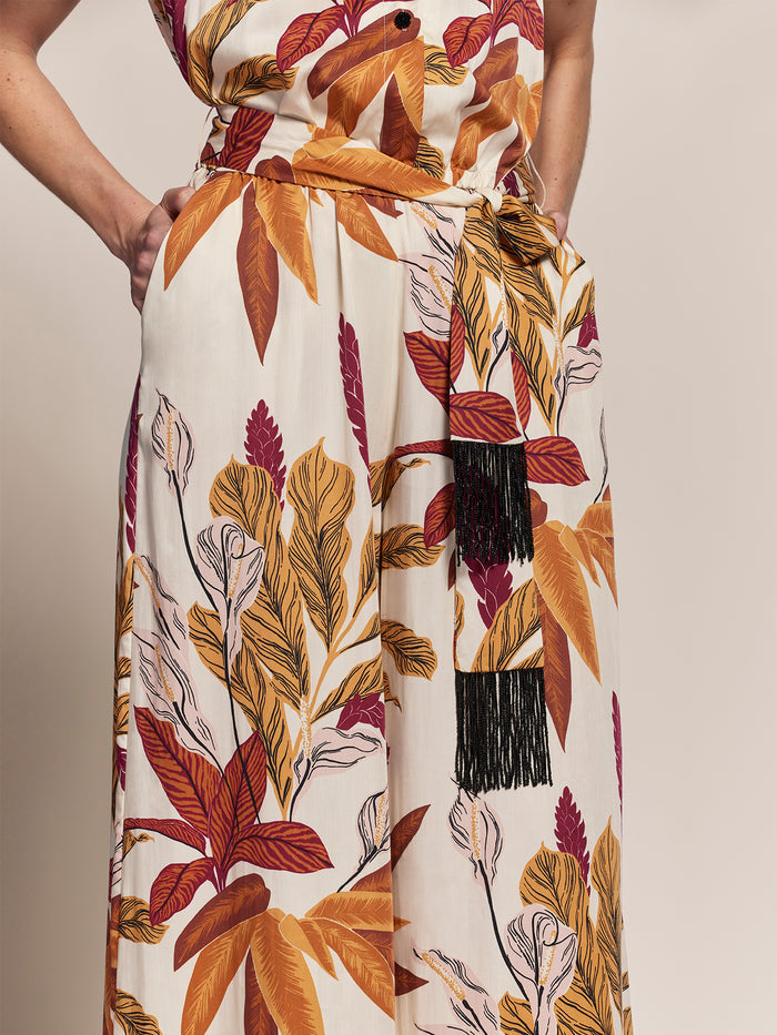 Tan leaf-print jumpsuit with black tassel belt, front view on model.