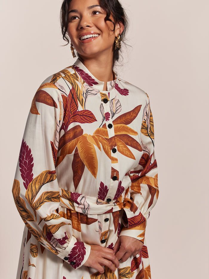 Pink floral-print midi dress, hands clasped, three-quarter view outdoors with autumn leaves.