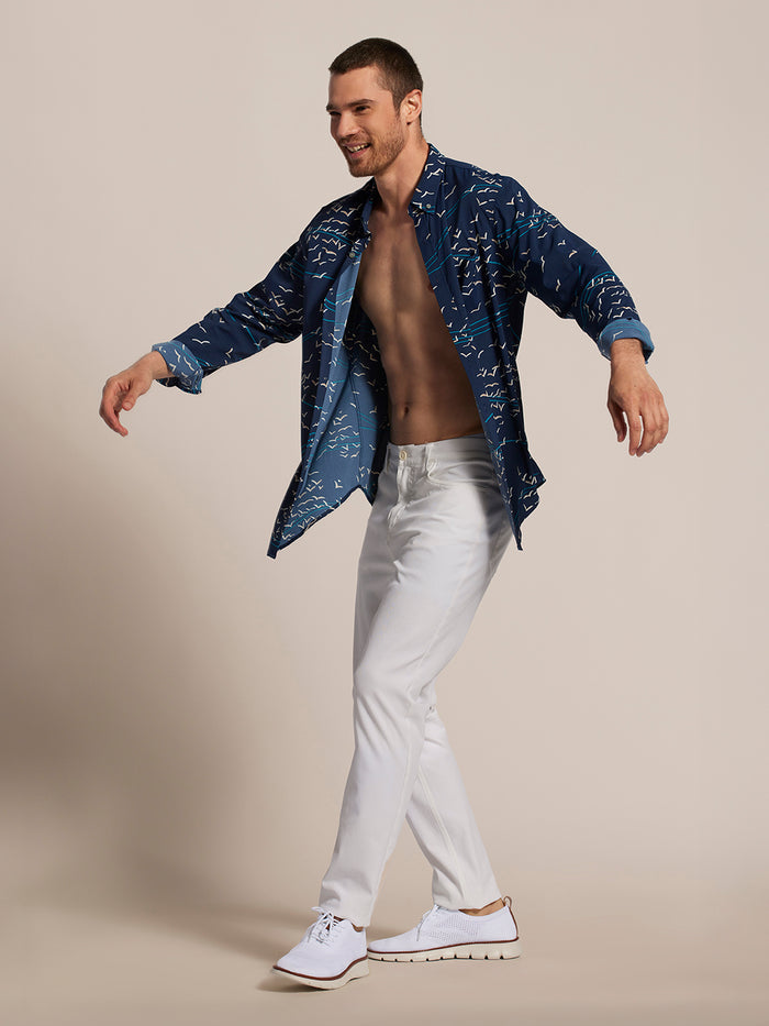 Navy shirt with white bird and blue stripe print, button-up, long sleeves with white pants and sneakers, front walking view.