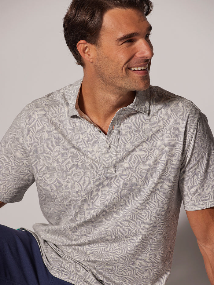 Light gray tapa-pattern polo shirt, man seated, looking sideways.