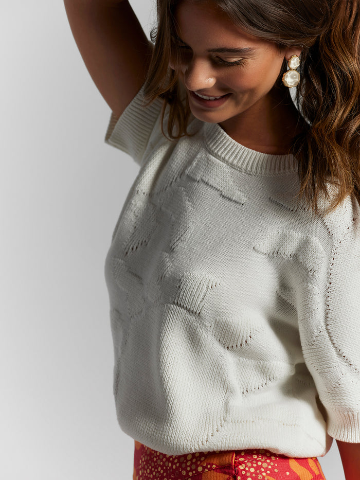 White jacquard sweater, red patterned skirt, statement earrings, front view.