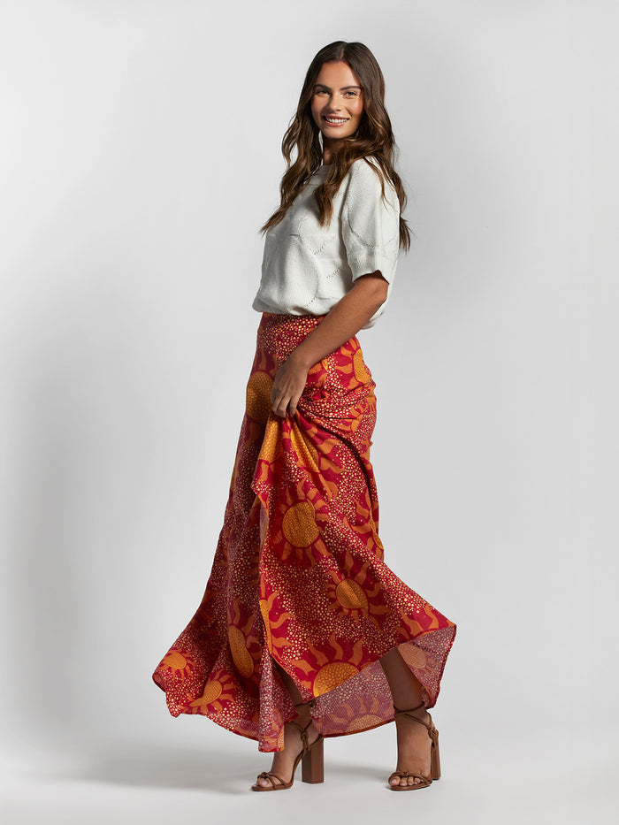 A woman wearing a white jacquard sweater and a maxi skirt with a geometric red and yellow pattern.