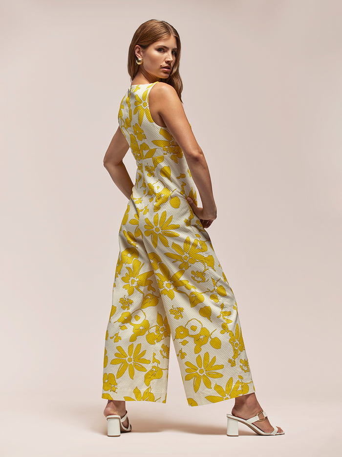 White and yellow floral-print jumpsuit, back view with white heels.