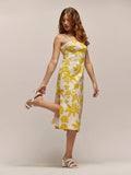 Yellow floral-print cotton dress, vintage sandals detail, woman holding her ankle.
