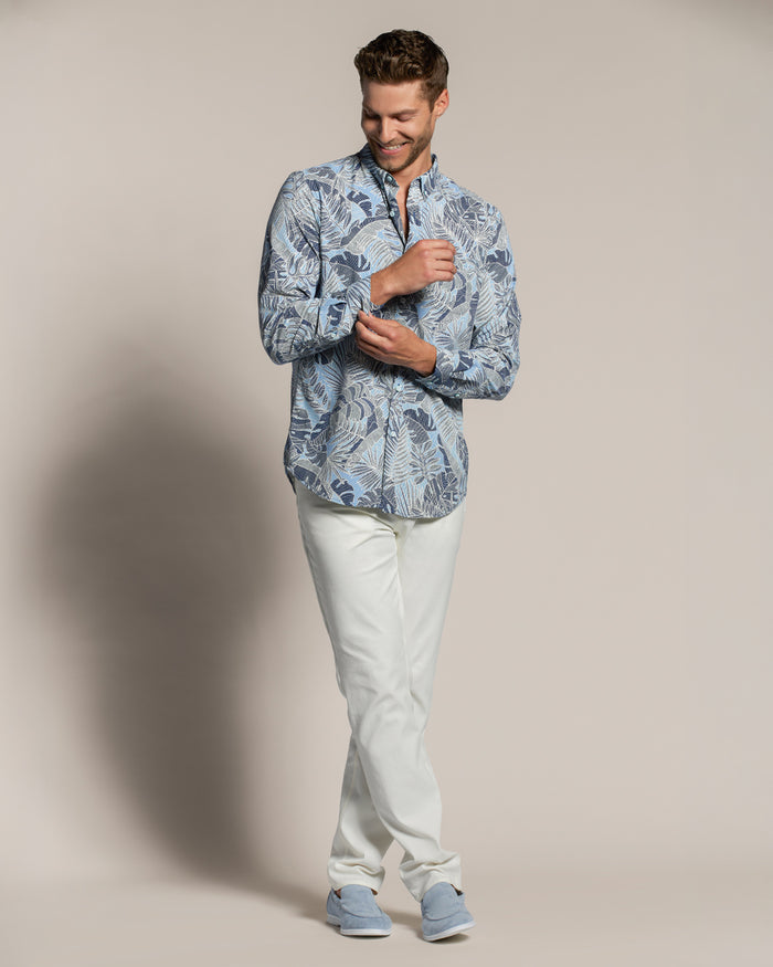 Blue and white tropical-print long-sleeve shirt, with white pants, arms crossed, front view shown in both images.