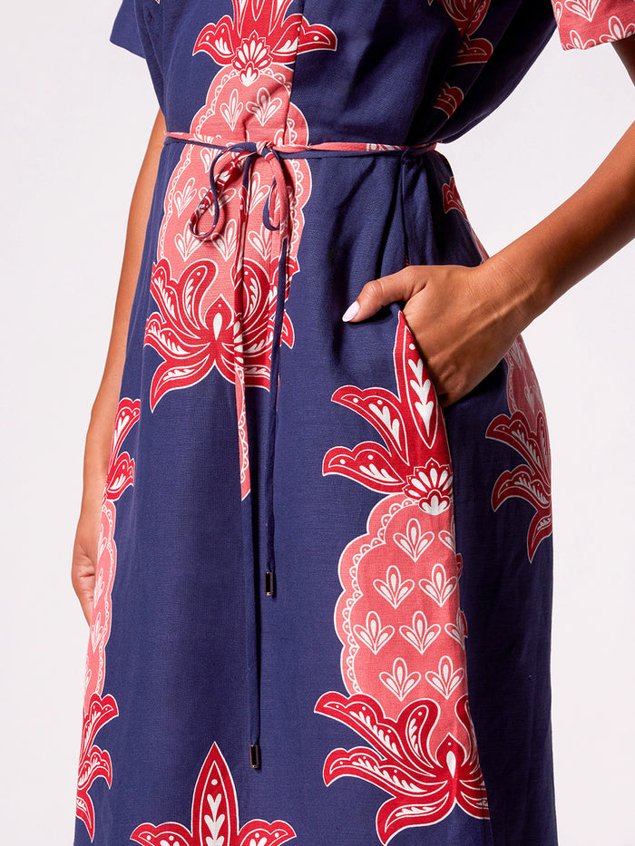 Blue dress with red and pink floral print, waist tie detail, hand in pocket view.