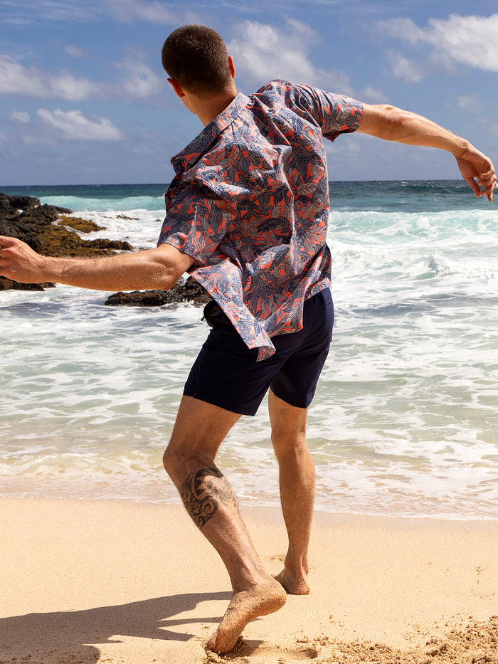 Blue palm-print short-sleeve shirt, front view, worn by man running barefoot on beach.