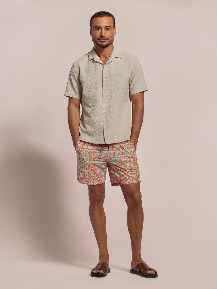 Beige short-sleeve shirt with Orange and white geometric-print swim shorts, front view.