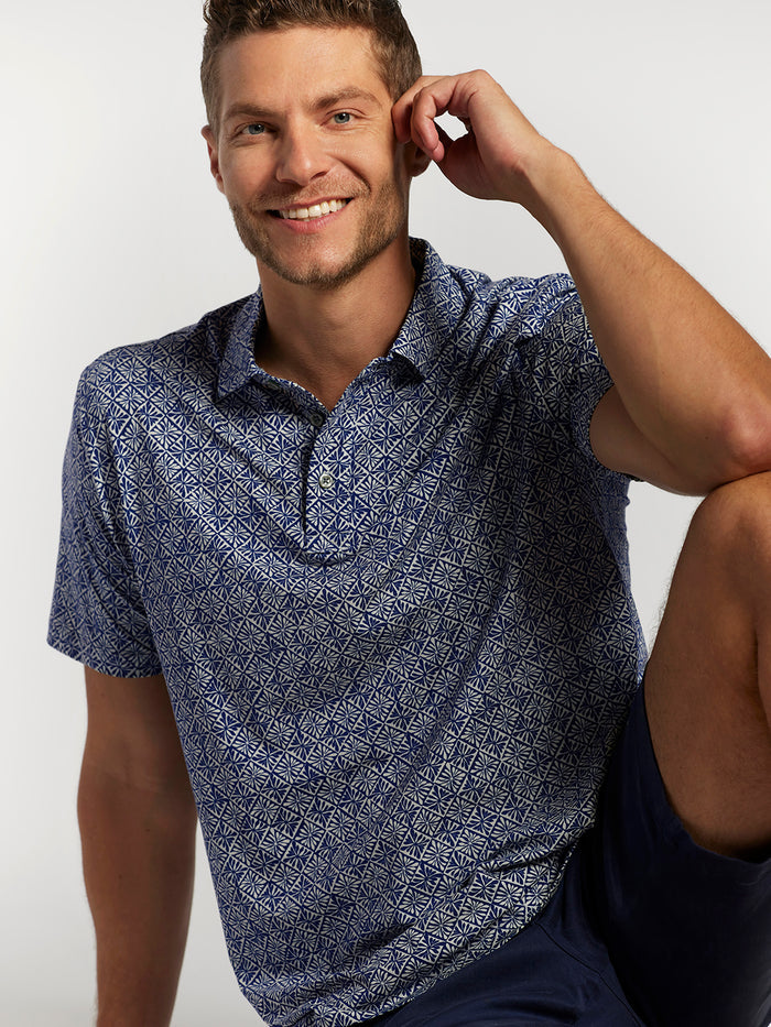 Blue polo shirt with white diamond pattern, and navy shorts, a model front seated view
