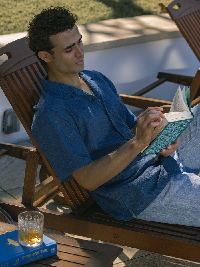 Blue with tile-print cabana shirt, relaxed outdoor view near breeze blocks.