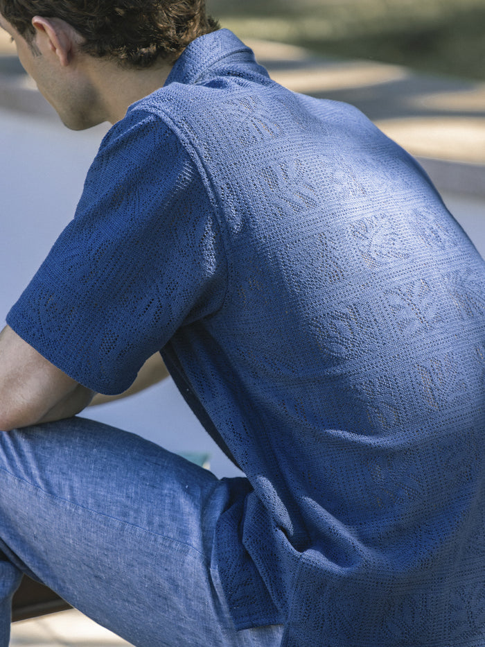Blue textured short-sleeve shirt and blue jeans, outdoor back side view.