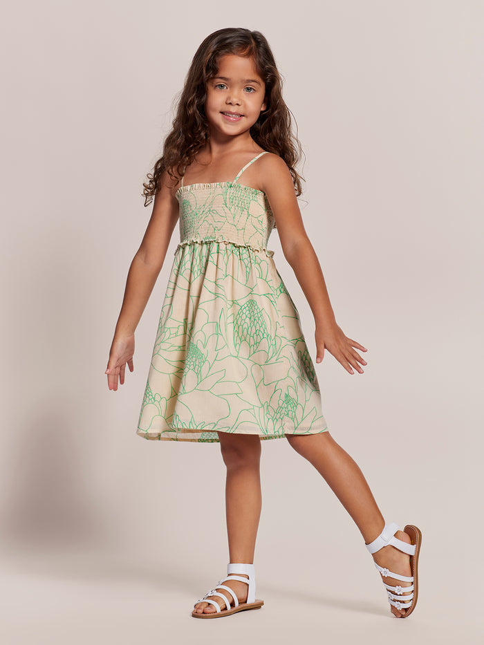 Girl with long brown hair and white sandals wearing green floral-print Adalei dress, front view.