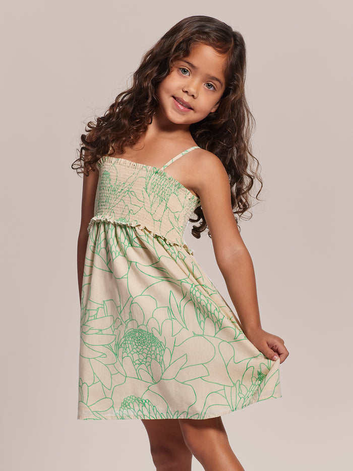 green floral cotton voile dress, girl holding skirt, plain background, front view.