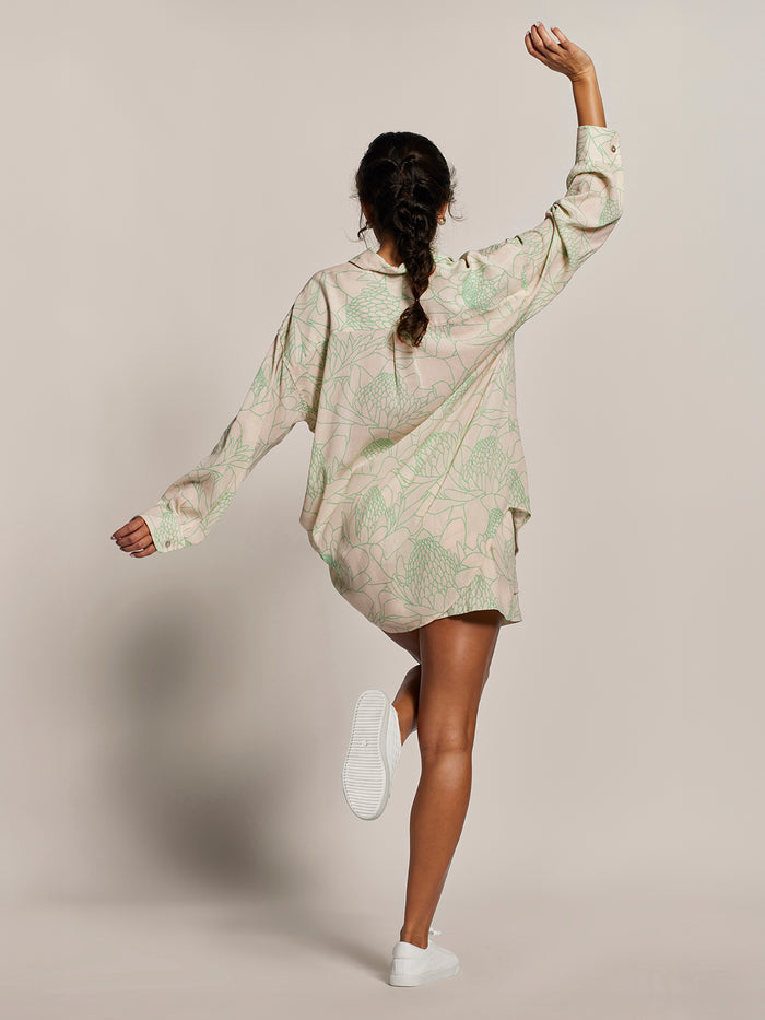 Cream relaxed-fit top and sneakers, front view, womans arm raised, braid visible.