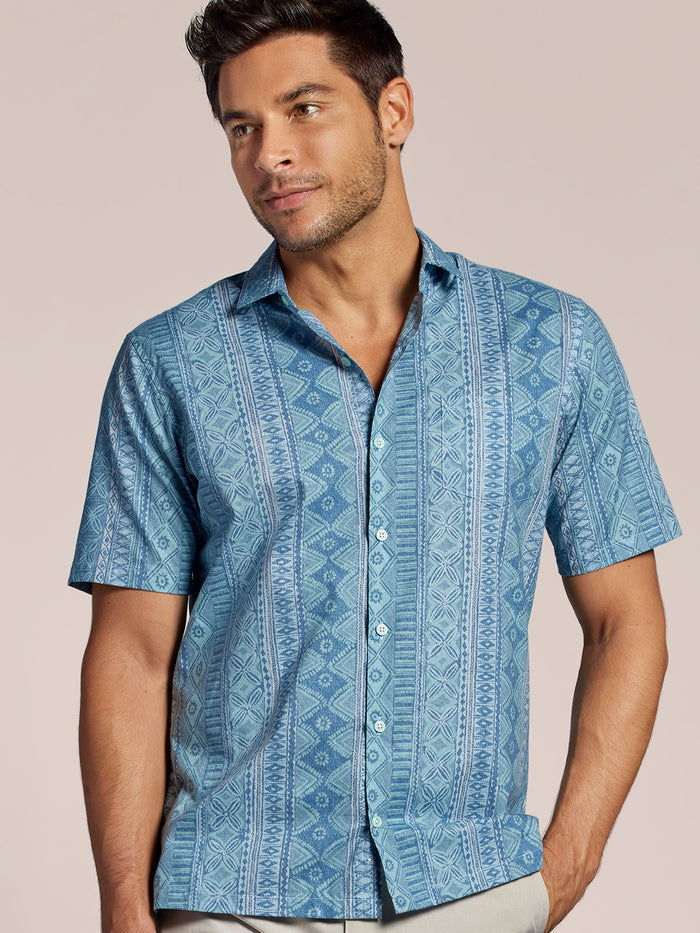 Blue geometric-print short-sleeve cotton button-up shirt with collar, side view of a man against plain background.