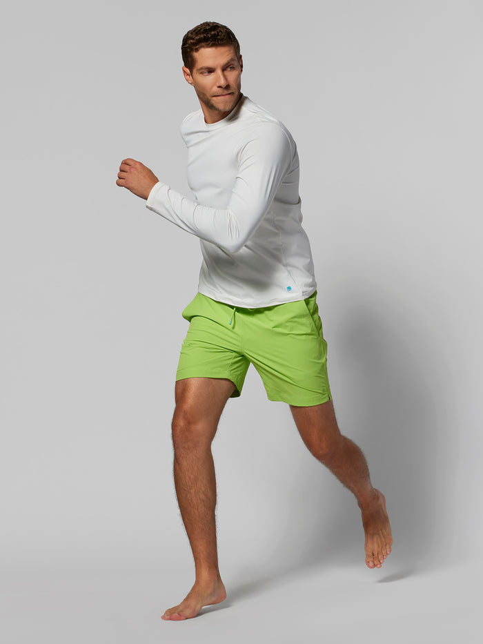 Bright green solid swim trunks with elastic waist, drawstring, Tradewind swim shorts, white shirt, barefoot, full-body.
