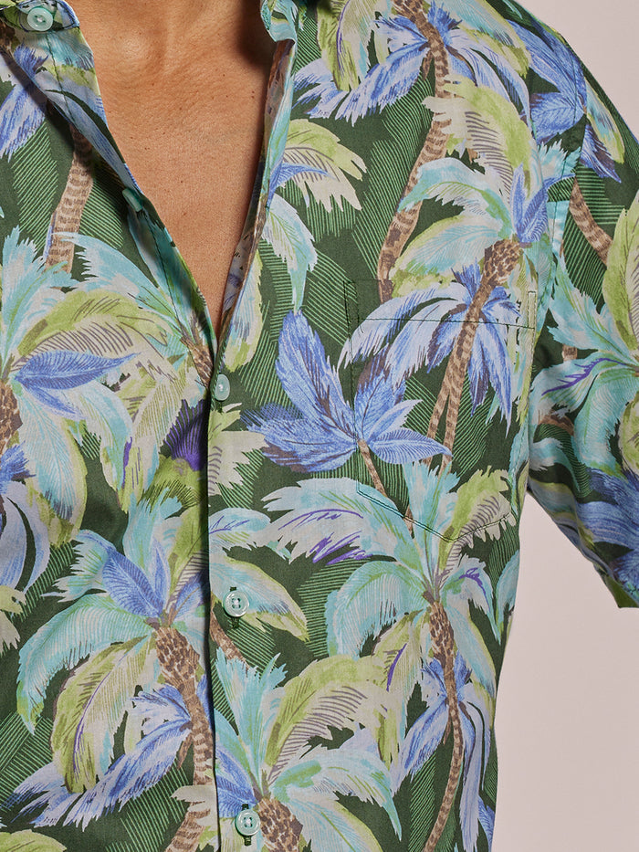 Green cotton shirt with blue palm tree print, partially unbuttoned, front view.