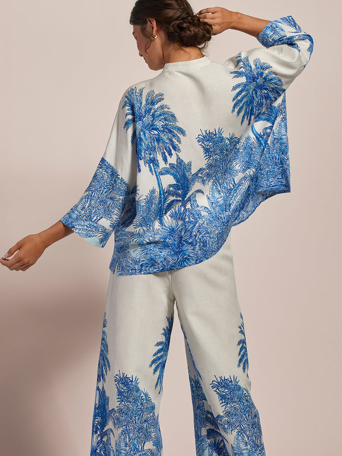 White with blue palm tree print top, back view, one arm raised.