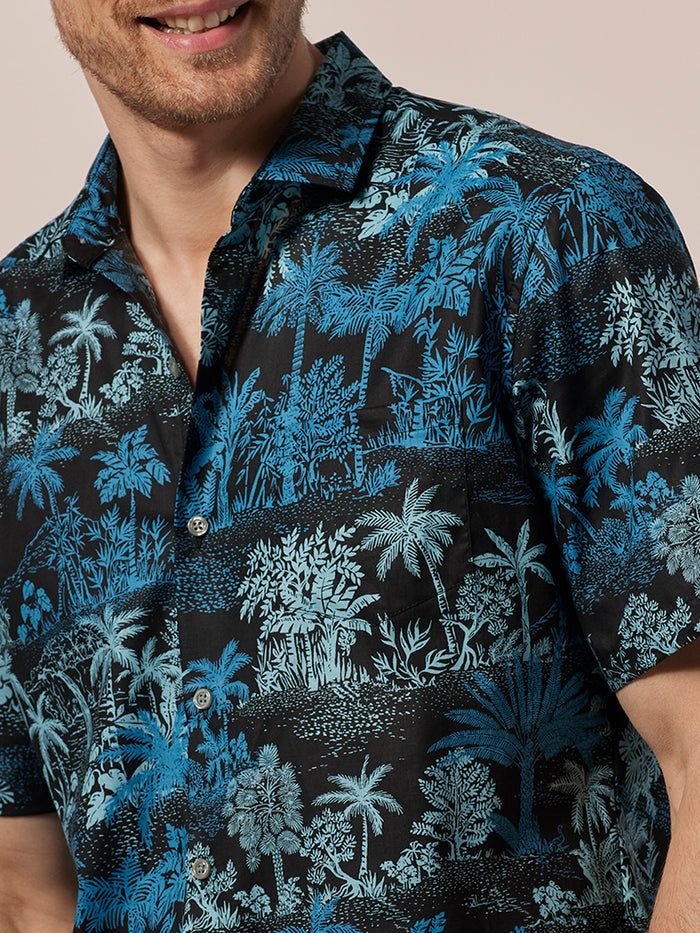 Black and blue palm tree-print short-sleeve shirt, front view with man smiling.
