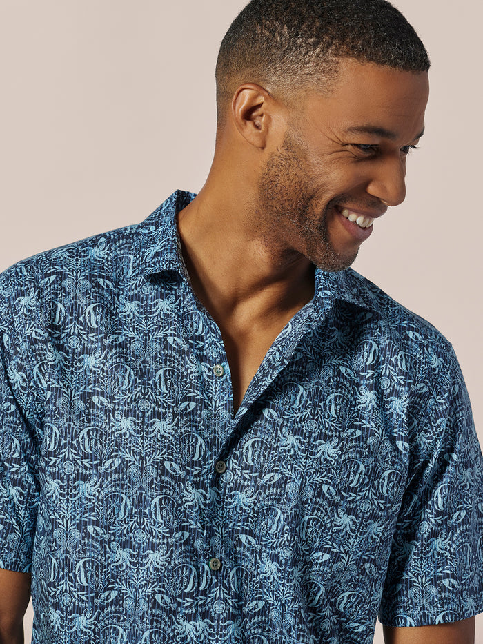Blue and white underwater-print button-up shirt, side view of man against light background.