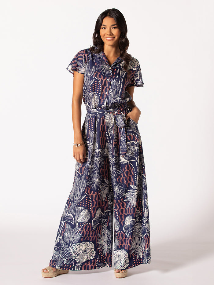 Blue and white patterned short-sleeve jumpsuit, wide legs, hands in pockets, front view.