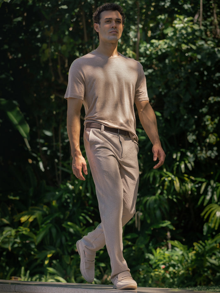 Light beige t-shirt and matching beige trousers, and shoes with a dark belt, set against a lush green background of foliage.
