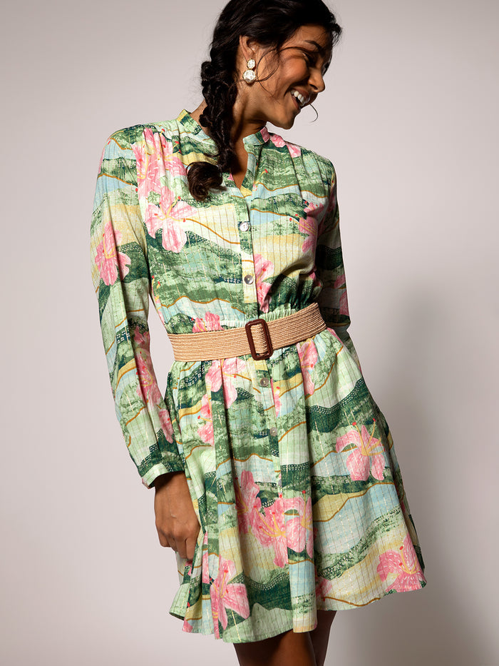 Green and pink floral-print sleeveless dress, woman smiling and looking down right.