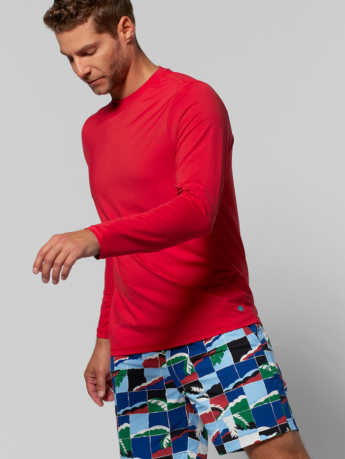 Bright red long-sleeve shirt and patterned swim trunks, side view, man looking down.