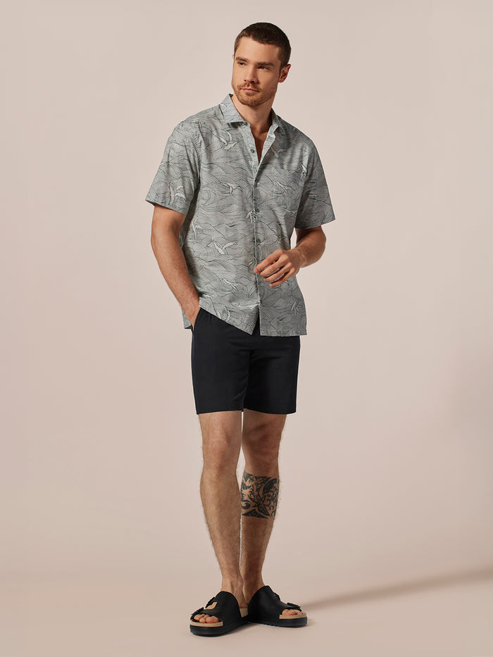 Blue whale-print cotton short-sleeve shirt on man, against a plain beige background.