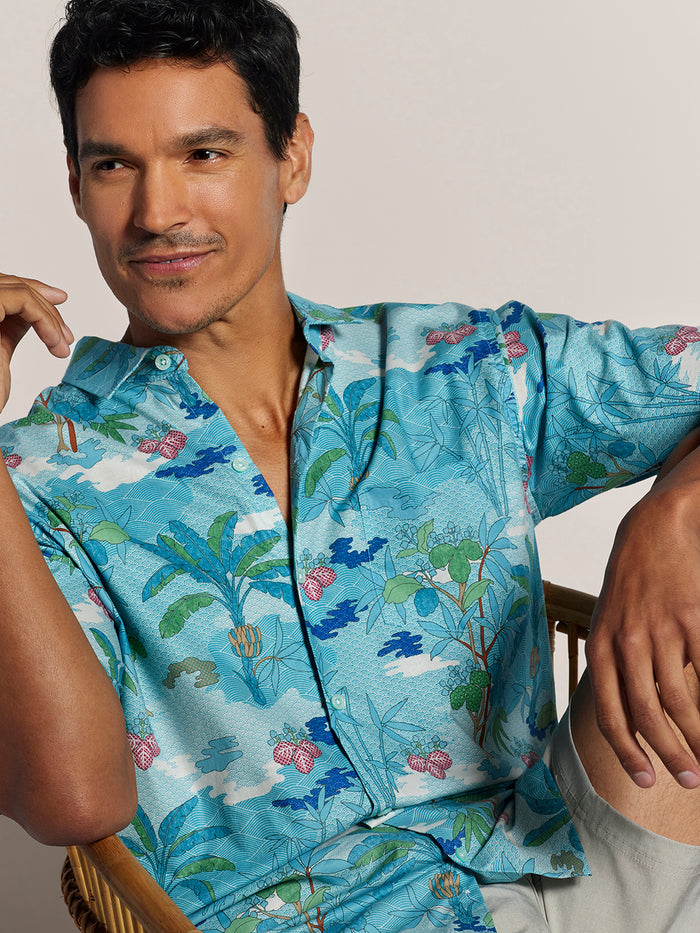 Blue/white abstract-print cotton shirt with beige shorts, side-seated view.